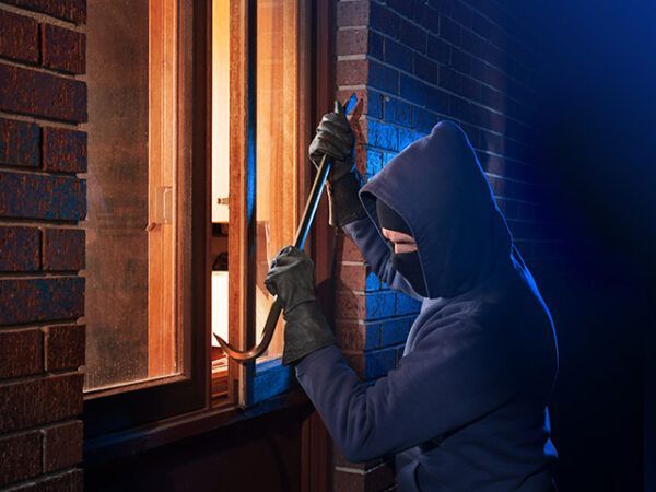 A burglar trying to get access into a property using a crowbar to pry a window open at night.