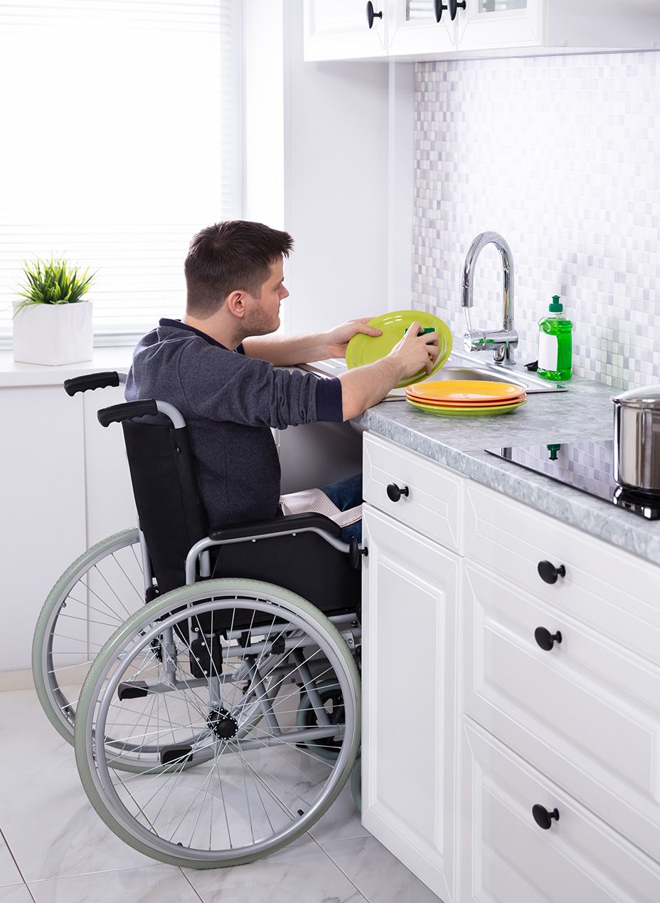 Disabled man sitting in his wheel chair and independently washing dishes at the kitchen sink.