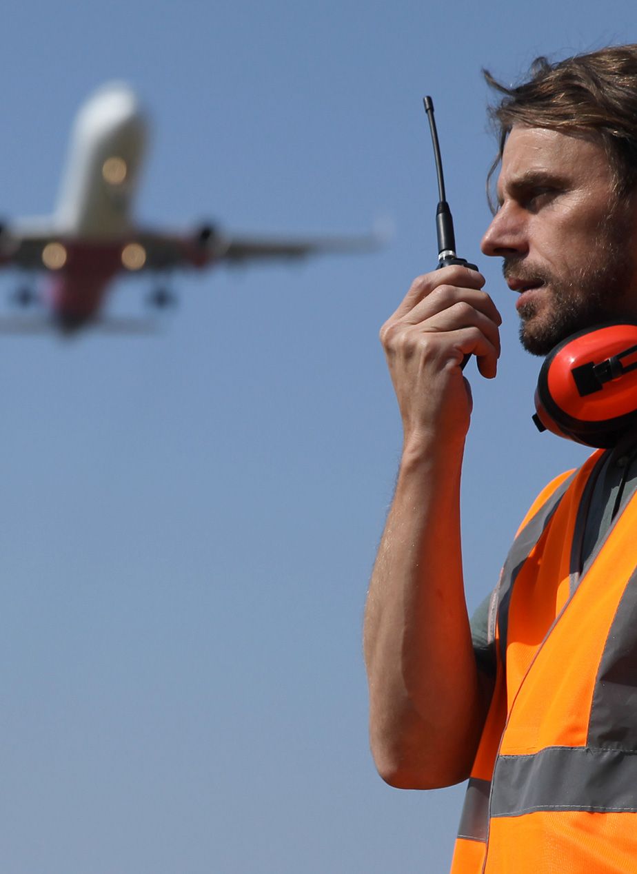 A man using a two-way-radio at an airport to communicate with workers.