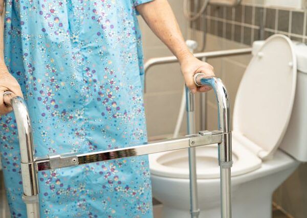 Elderly lady using a disability walker in a residential bathroom fitted with disability grab rails for support